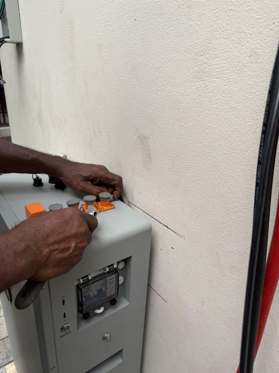Close-up of hands adjusting DC disconnect breaker terminals on top of a battery cabinet