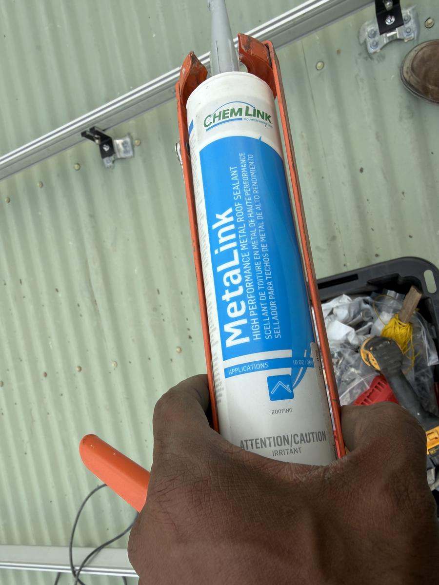 Tube of Chem Link MetaLink metal roof sealant in a caulking gun, used to seal a solar mounting bracket on a corrugated roof