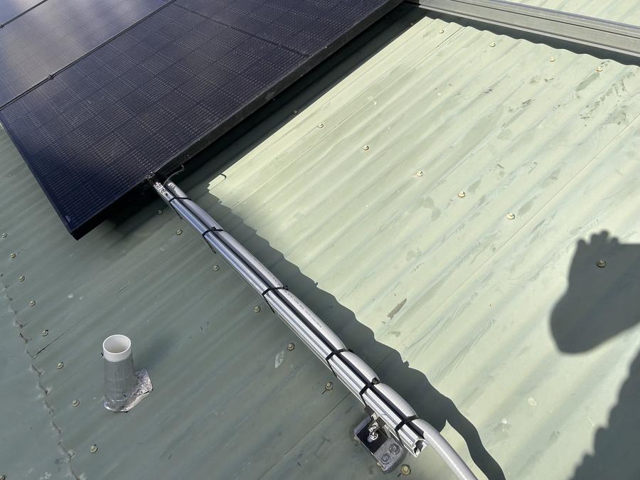 Close-up of solar panel mounting rail and conduit run on a metal roof
